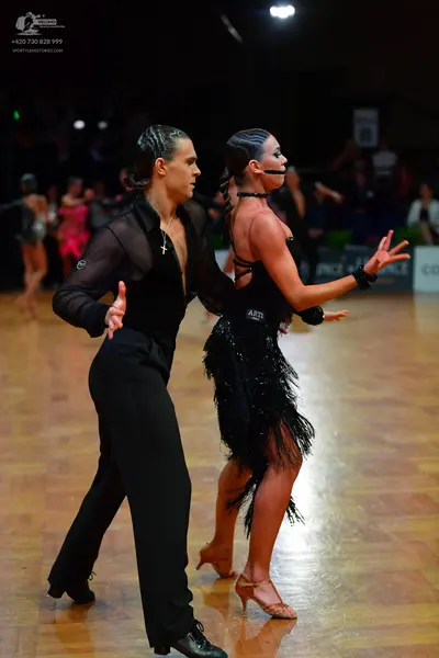 Dancesport competitor: Male dancer: black sheer long-sleeved shirt, black trousers, and a silver cross 