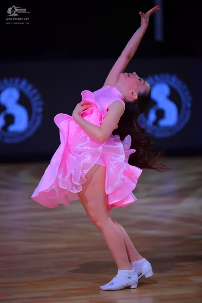 Dancesport competitor: Female dancer: bright pink latin dress with voluminous ruffled layers, likely ma