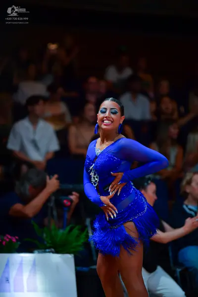 Dancesport competitor: Female dancer: royal blue latin dress with long sleeves, sheer mesh panels, and 