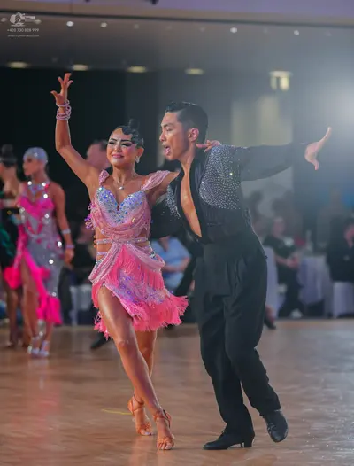 Dancesport competitor: Foreground female dancer: pink latin dance dress with sequins and fringe, and pi