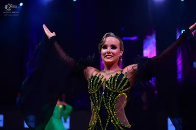 Dancesport competitor: Female dancer in foreground: black latin dress with gold sequin patterns, nude m