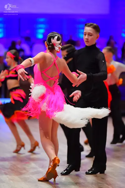 Dancesport competitor: Foreground female dancer: pink Latin dress with white feather-like fringe and cr