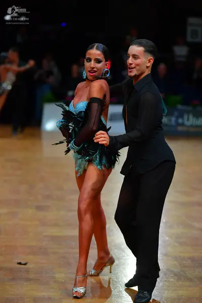 Dancesport competitor: Female dancer: teal latin dress with dark feathers/fringe and sequins