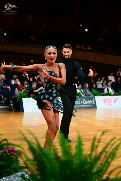 Dancesport competitor: Female dancer: black latin dress with a vibrant teal, blue, and gold pattern res