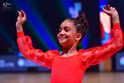 Dancesport competitor: Female dancer: red Latin dress with sheer long sleeves decorated with large red 