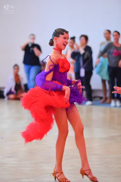 Dancesport competitor: Female dancer: purple Latin dance dress with long, sheer sleeves, a red fabric f