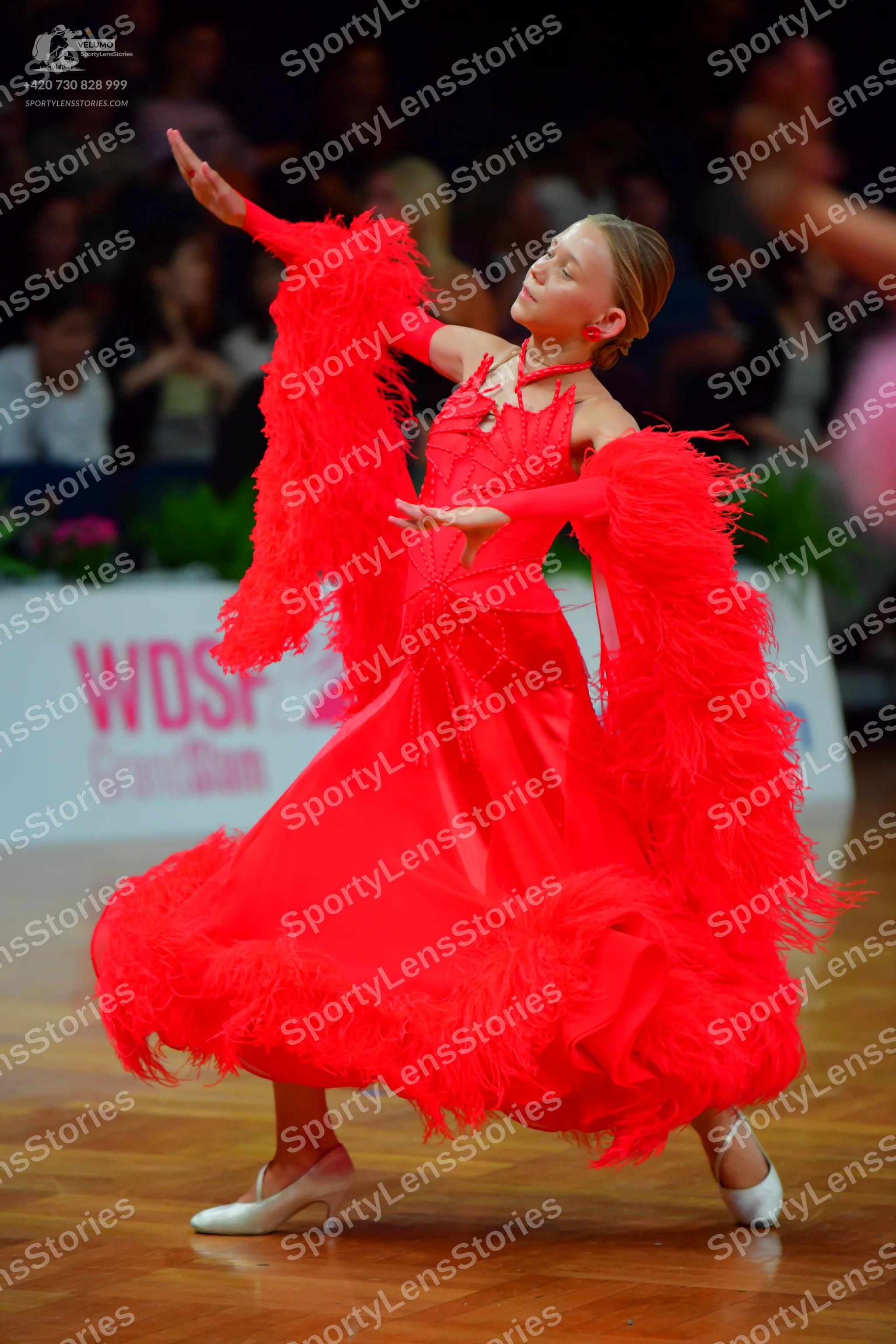 Dancesport competitor: Female dancer: red latin dress with voluminous red feather-like fringe on the sl
