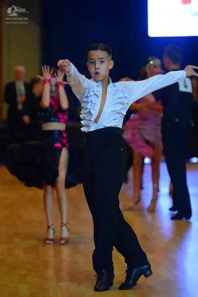 Dancesport competitor: Male dancer in foreground: white long-sleeved shirt with ruffles on the front, b