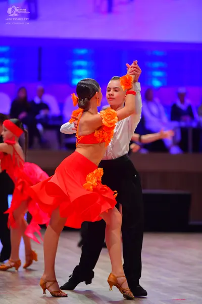Dancesport competitor: Female dancer: red and orange two-piece Latin costume featuring a crop top and s