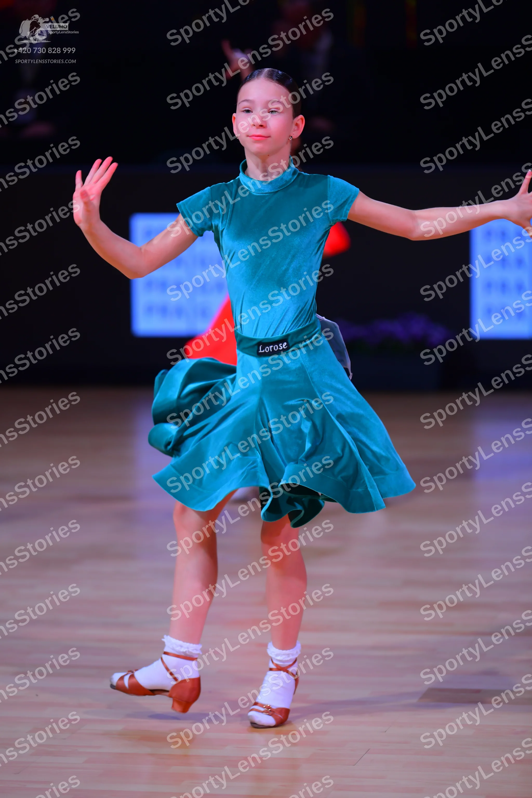 Dancesport competitor: Female dancer: teal satin-like dress with short sleeves, a high neck, and a flar