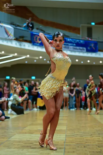 Dancesport competitor: Female dancer in foreground: gold Latin dance dress with sequins and fringe, and