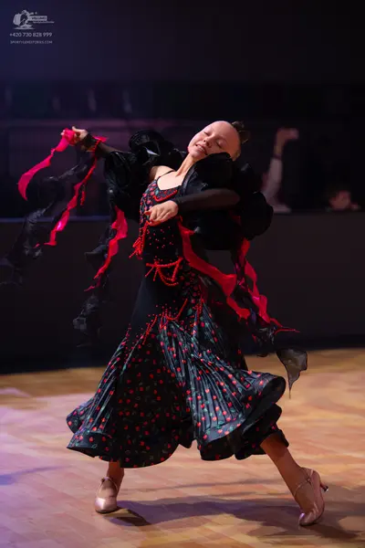 Dancesport competitor: Female dancer: black ballroom dress with red patterns, featuring long, flowing r