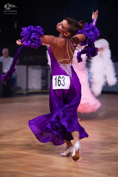 Dancesport competitor: Female dancer 1: purple ballroom dress with satin-like fabric, large ruffled sle