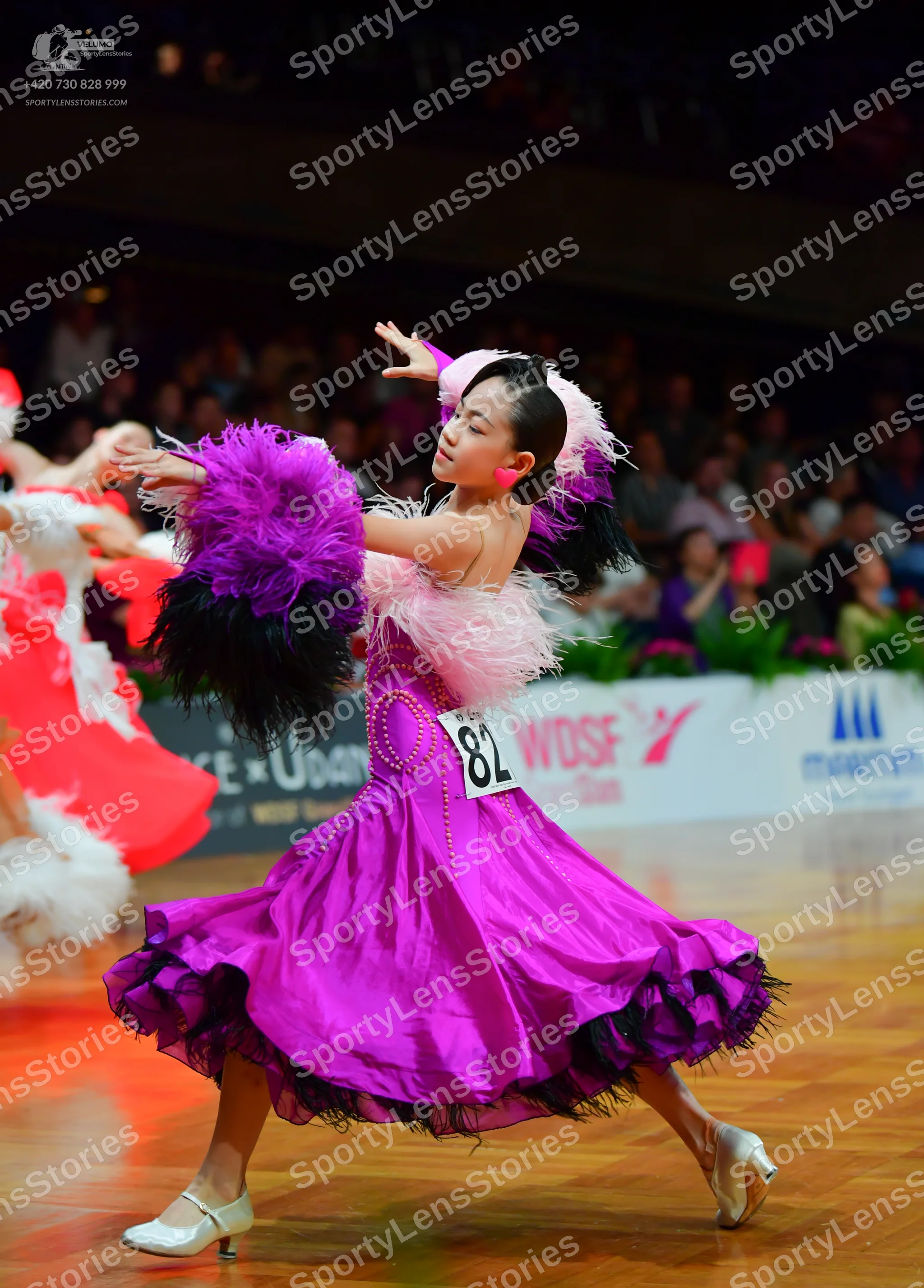 Dancesport competitor: Female dancer: magenta satin-like dress with a full, layered skirt featuring bla