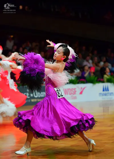 Dancesport competitor: Female dancer: magenta satin-like dress with a full, layered skirt featuring bla