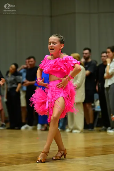 Dancesport competitor: Female dancer: bright pink latin dress with a ruffled neckline and a feathered/f