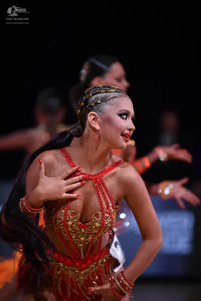 Dancesport competitor: Female dancer in foreground: red and gold Latin dance dress, heavily embellished