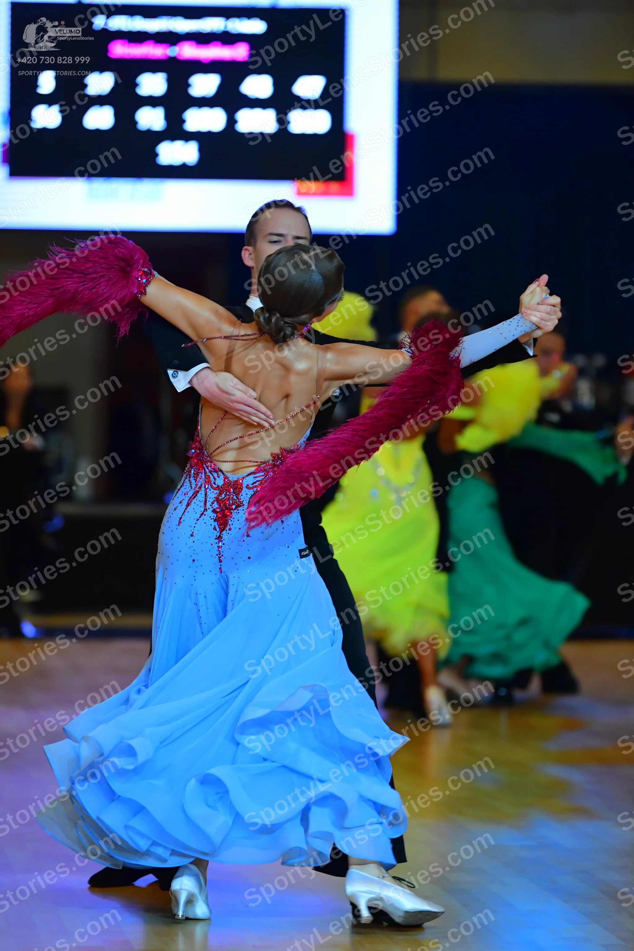 Dancesport competitor: Female dancer in foreground: light blue ballgown with a voluminous, ruffled skir