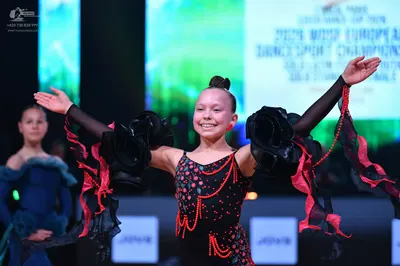 Dancesport competitor: Female dancer in foreground: black latin dance dress with red and pink sequined 