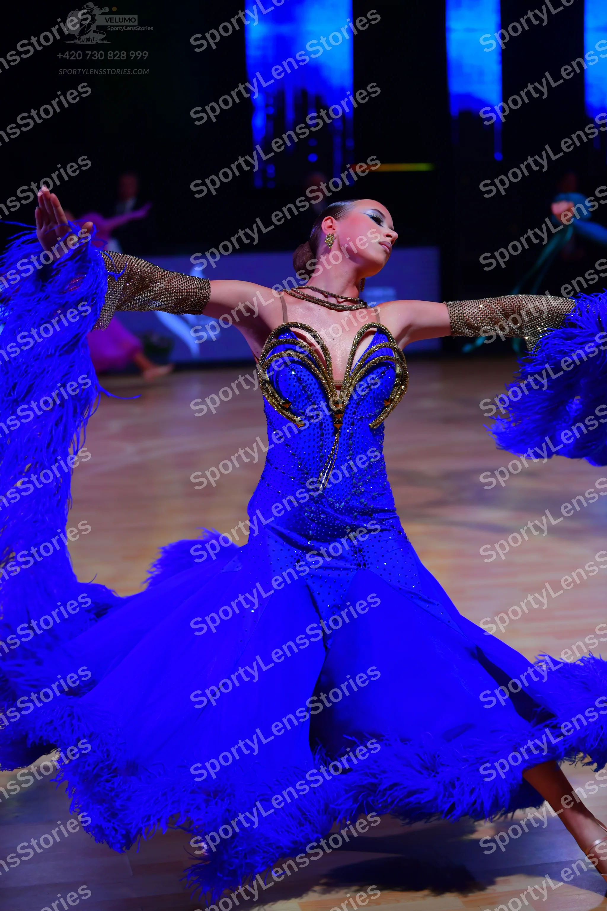 Dancesport competitor: Female dancer: bright blue Latin dance dress featuring blue feather trim on the