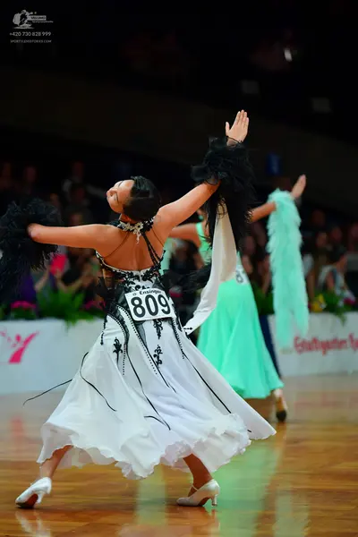 Dancesport competitor: Female dancer in foreground: white ballgown with black lace/sequin detailing on 