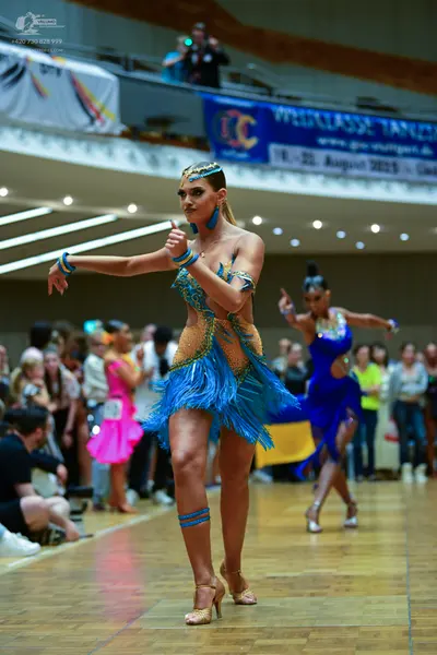 Dancesport competitor: Female dancer 1: blue and gold latin dress with sequins and blue fringe, paired 