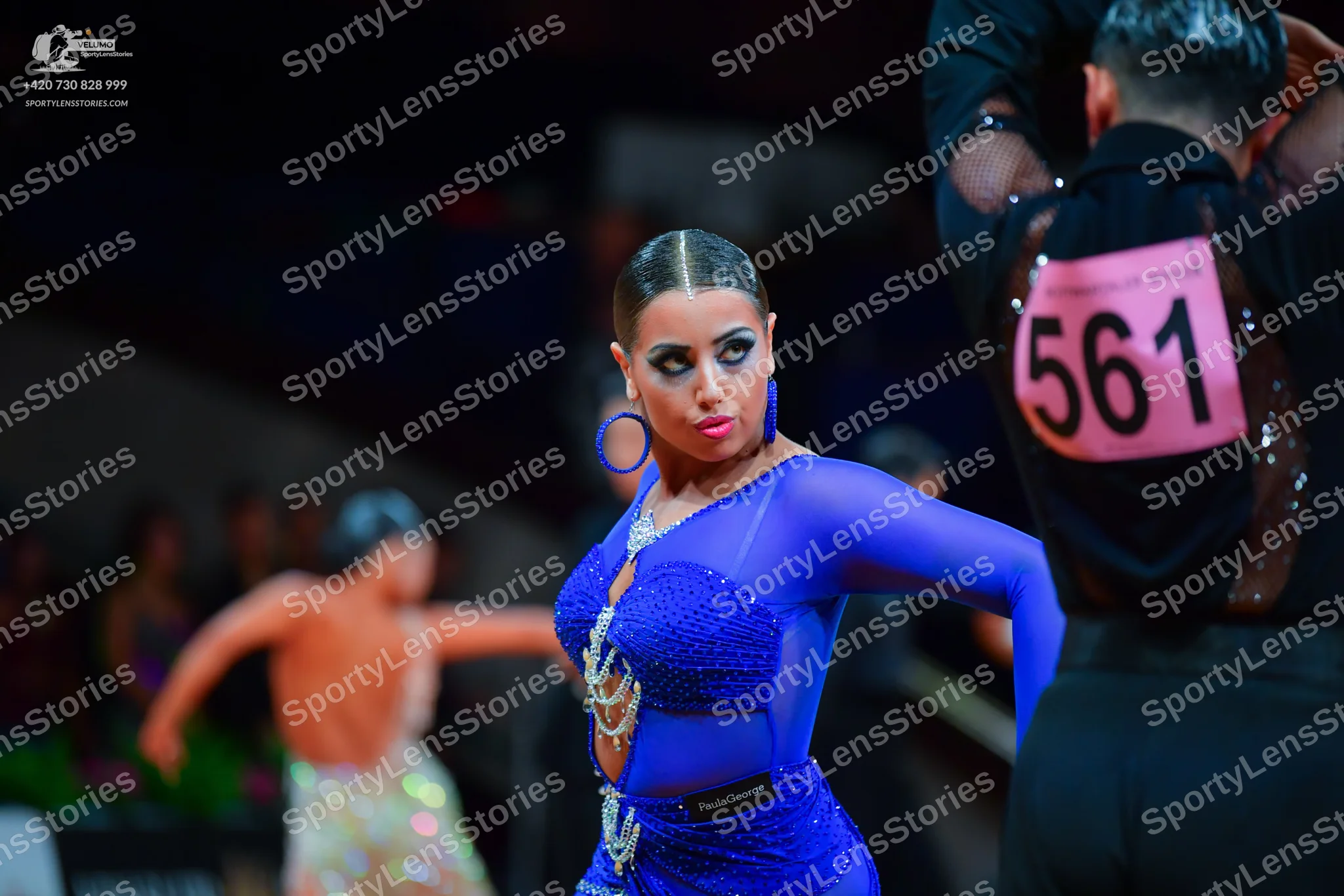 Dancesport competitor: Female dancer: blue latin dress with long sheer sleeves, blue sequins, and silve