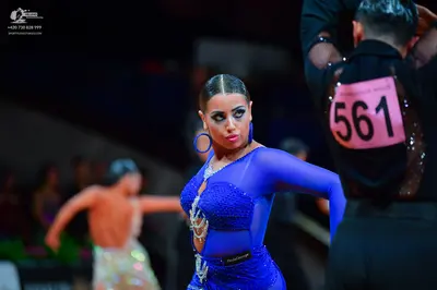 Dancesport competitor: Female dancer: blue latin dress with long sheer sleeves, blue sequins, and silve