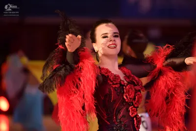 Dancesport competitor: Female dancer: black latin dress with red feather accents and red floral embelli
