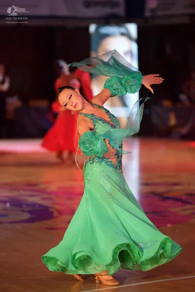 Dancesport competitor: Female dancer in foreground: emerald green ballroom gown featuring a sequined bo