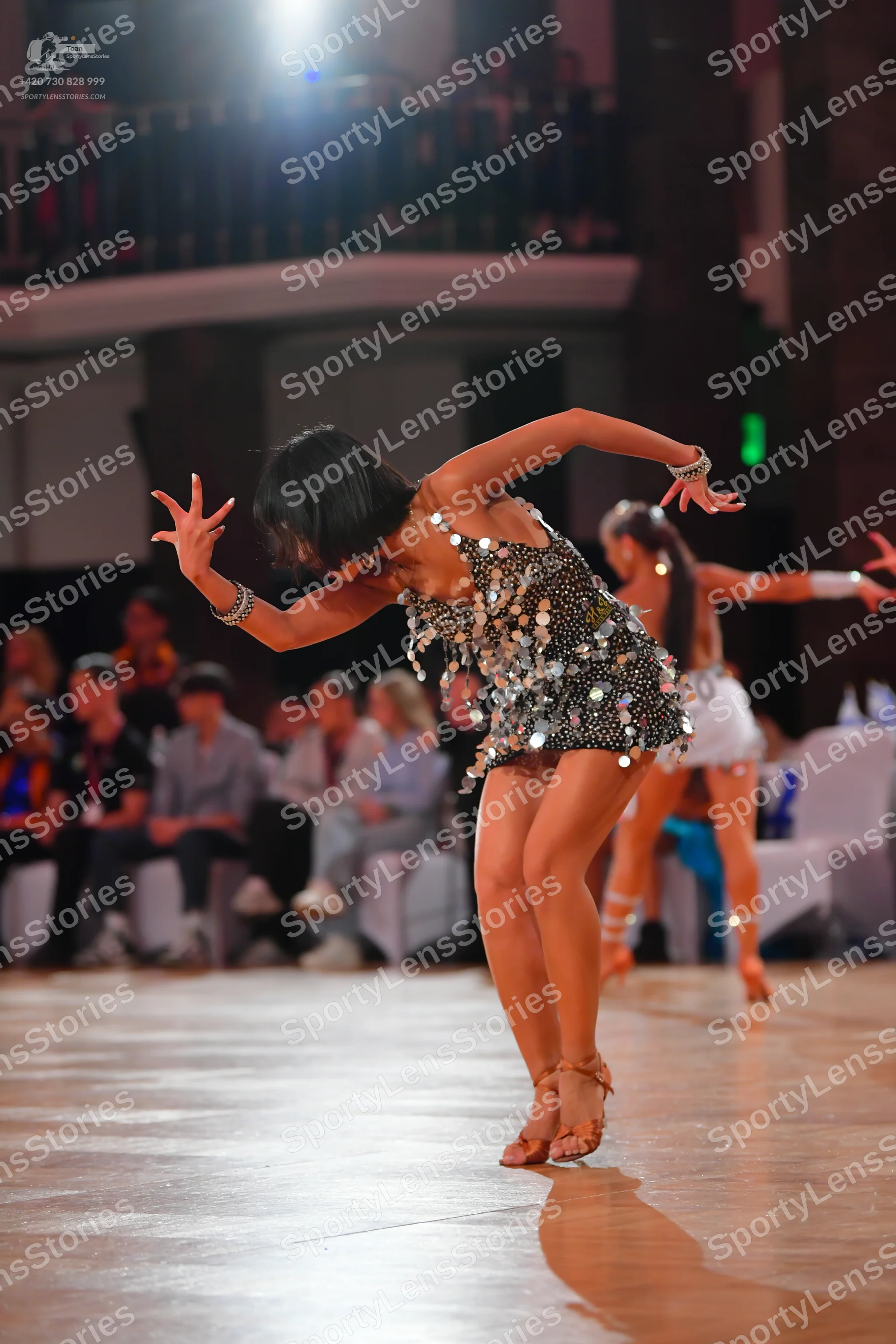 Dancesport competitor: Female dancer in foreground: dark latin dress covered in large, reflective silve