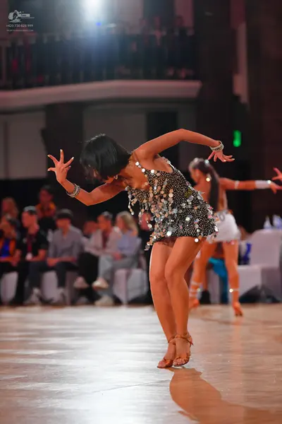 Dancesport competitor: Female dancer in foreground: dark latin dress covered in large, reflective silve