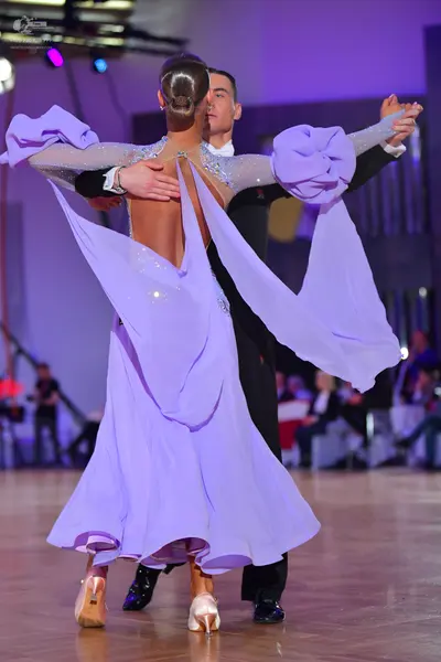 Dancesport competitor: Female dancer: light purple ballroom dress with long sleeves, an open back, and 