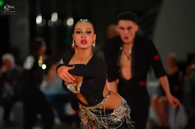 Dancesport competitor: Female dancer: black Latin-style costume with long sleeves and heavy silver sequ