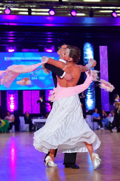 Dancesport competitor: Female dancer: white ballroom gown with a flowing skirt and a large, light pink/