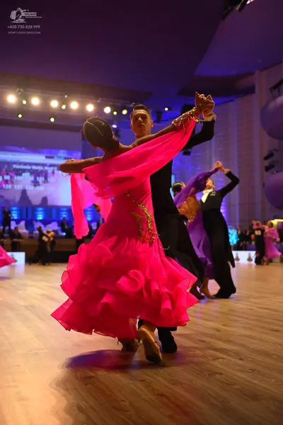 Dancesport competitor: Foreground female dancer: bright pink Latin dance dress with a layered, ruffled 
