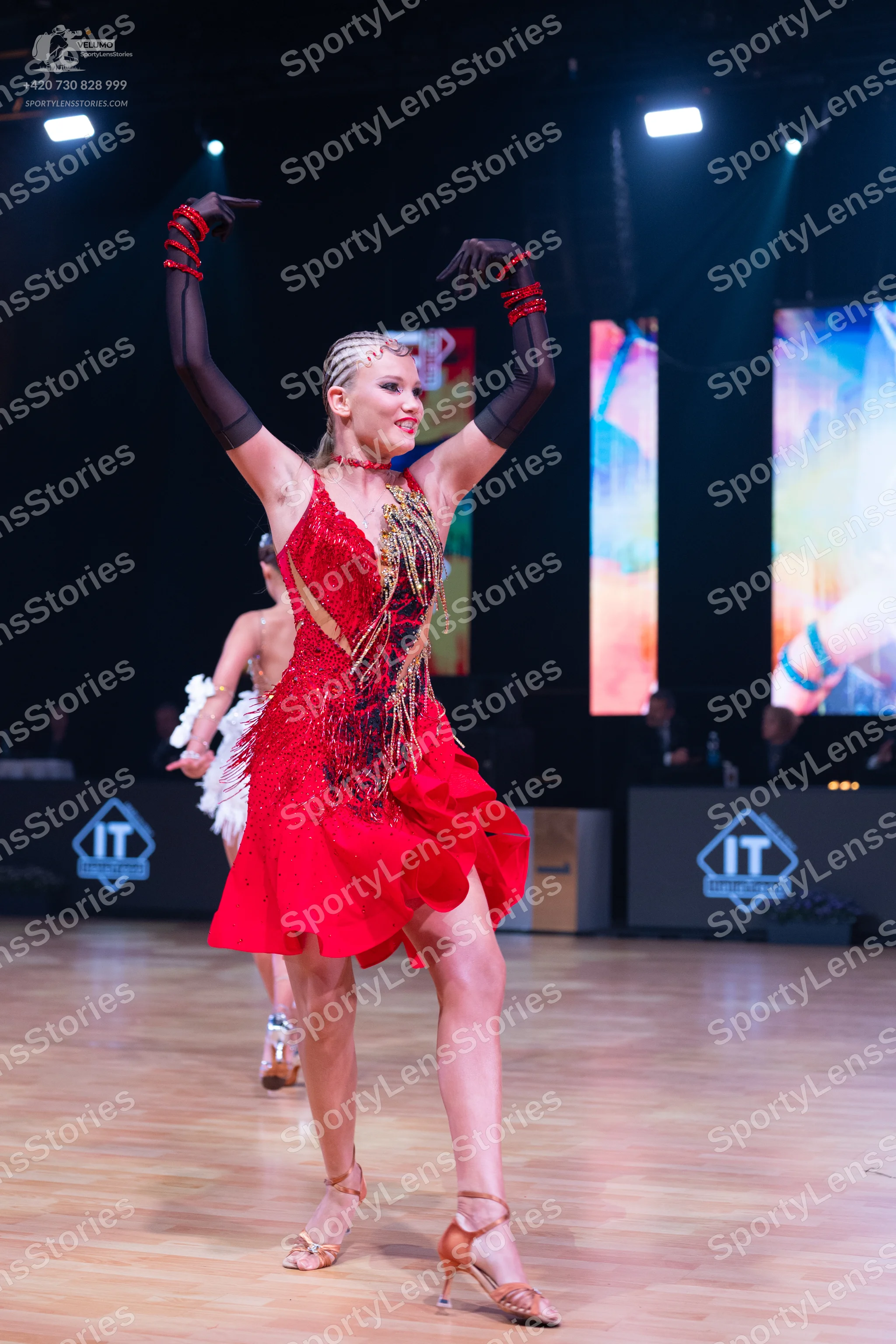 Dancesport competitor: Female dancer in foreground: red latin dress with a sequined bodice and a ruffle