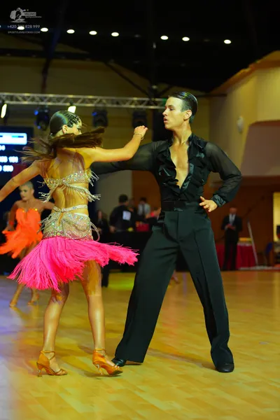 Dancesport competitor: Female dancer (foreground): gold sequin top with bright pink fringe skirt and go