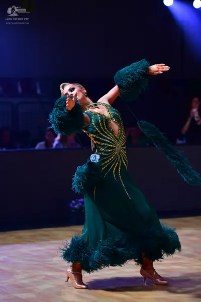 Dancesport competitor: Female dancer: emerald green ballgown with a gold sequin sunburst pattern on the