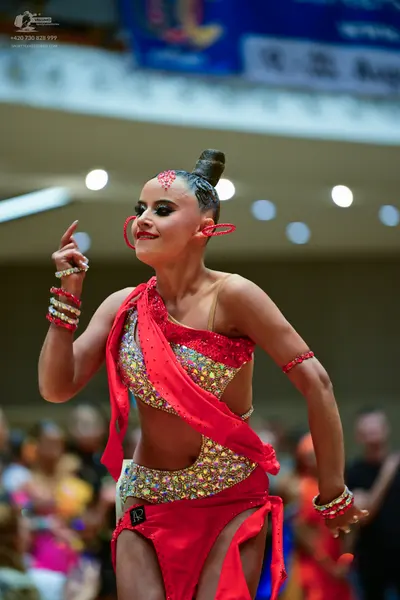 Dancesport competitor: Female dancer: red latin dress with gold and silver sequins, featuring an asymme