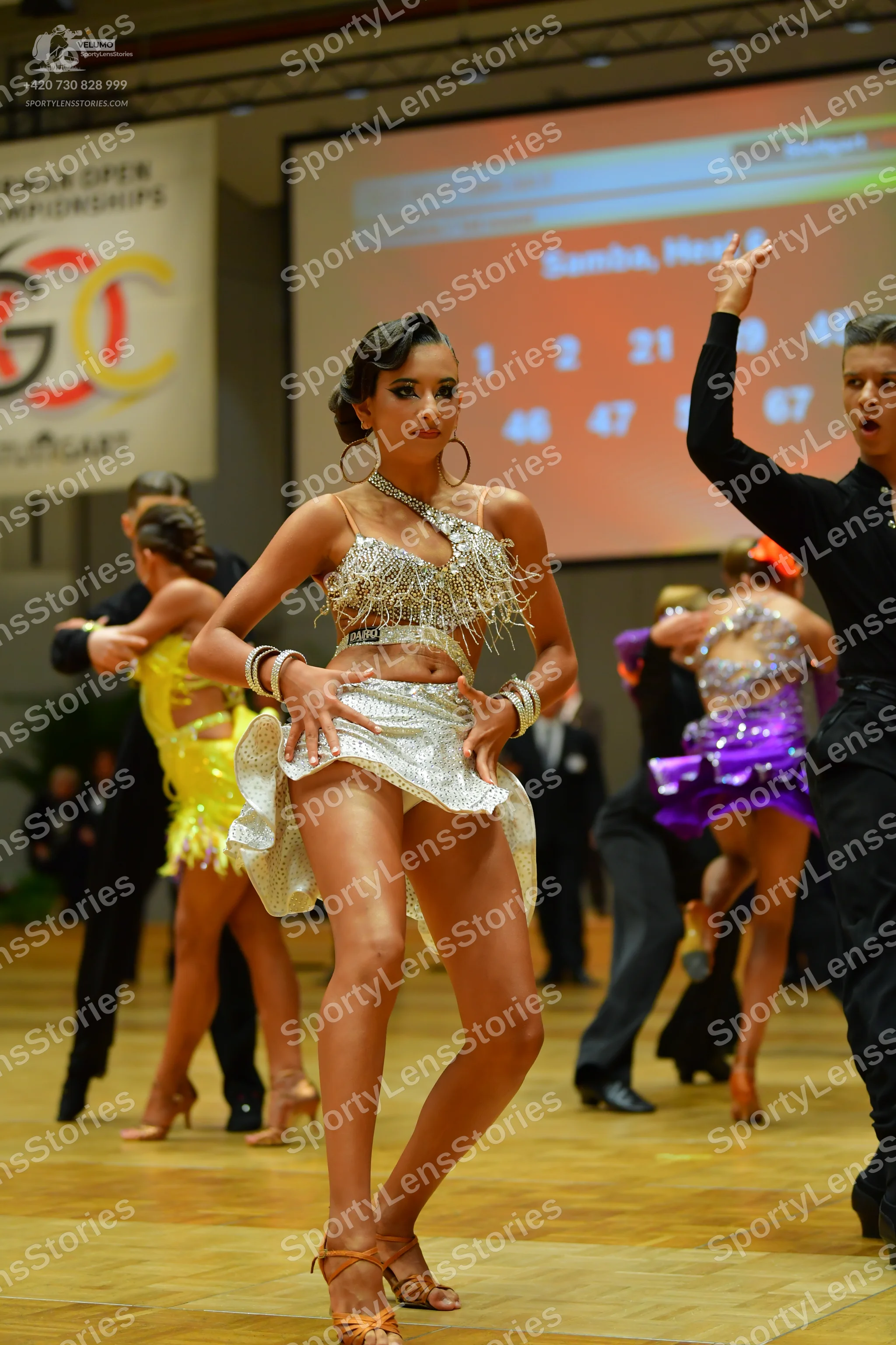 Dancesport competitor: Female dancer (foreground): silver sequin Latin dress with an asymmetrical one-s
