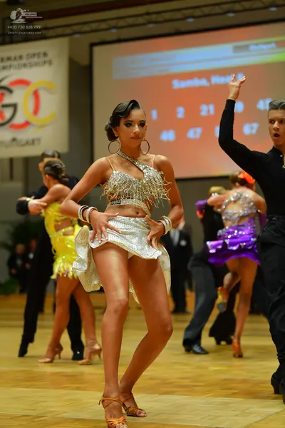 Dancesport competitor: Female dancer (foreground): silver sequin Latin dress with an asymmetrical one-s