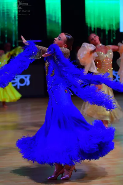 Dancesport competitor: Female dancer in foreground: blue latin dress with large blue feather trim on th