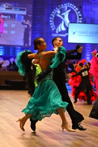 Dancesport competitor: Main female dancer: teal Latin dress with black feather-like trim on the arms, a