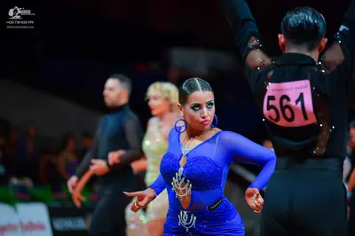 Dancesport competitor: Female dancer in foreground: blue latin dress with sequins, long sleeves, and rh