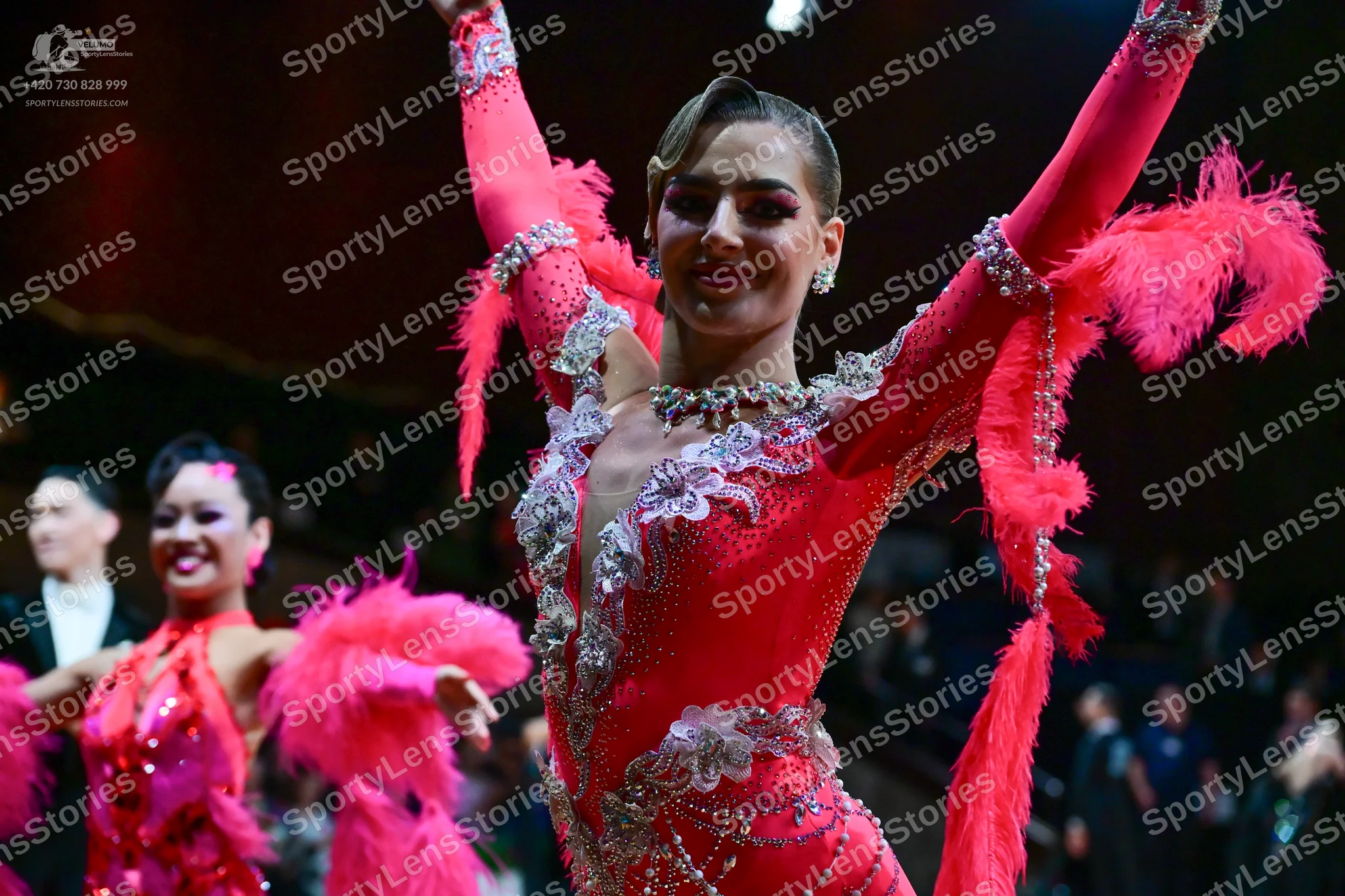Dancesport competitor: Foreground female dancer: bright pink latin dress with sequins, silver/crystal e