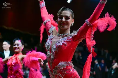 Dancesport competitor: Foreground female dancer: bright pink latin dress with sequins, silver/crystal e