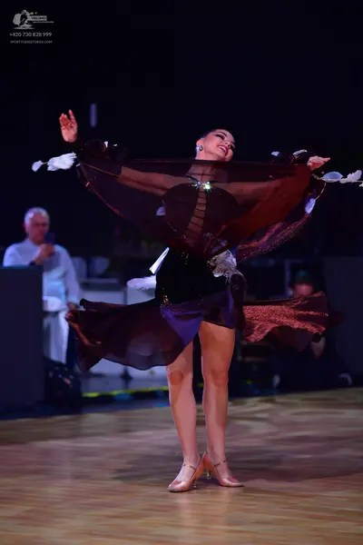 Dancesport competitor: Female dancer: burgundy Latin dance dress with large, flowing, sheer sleeves/cap