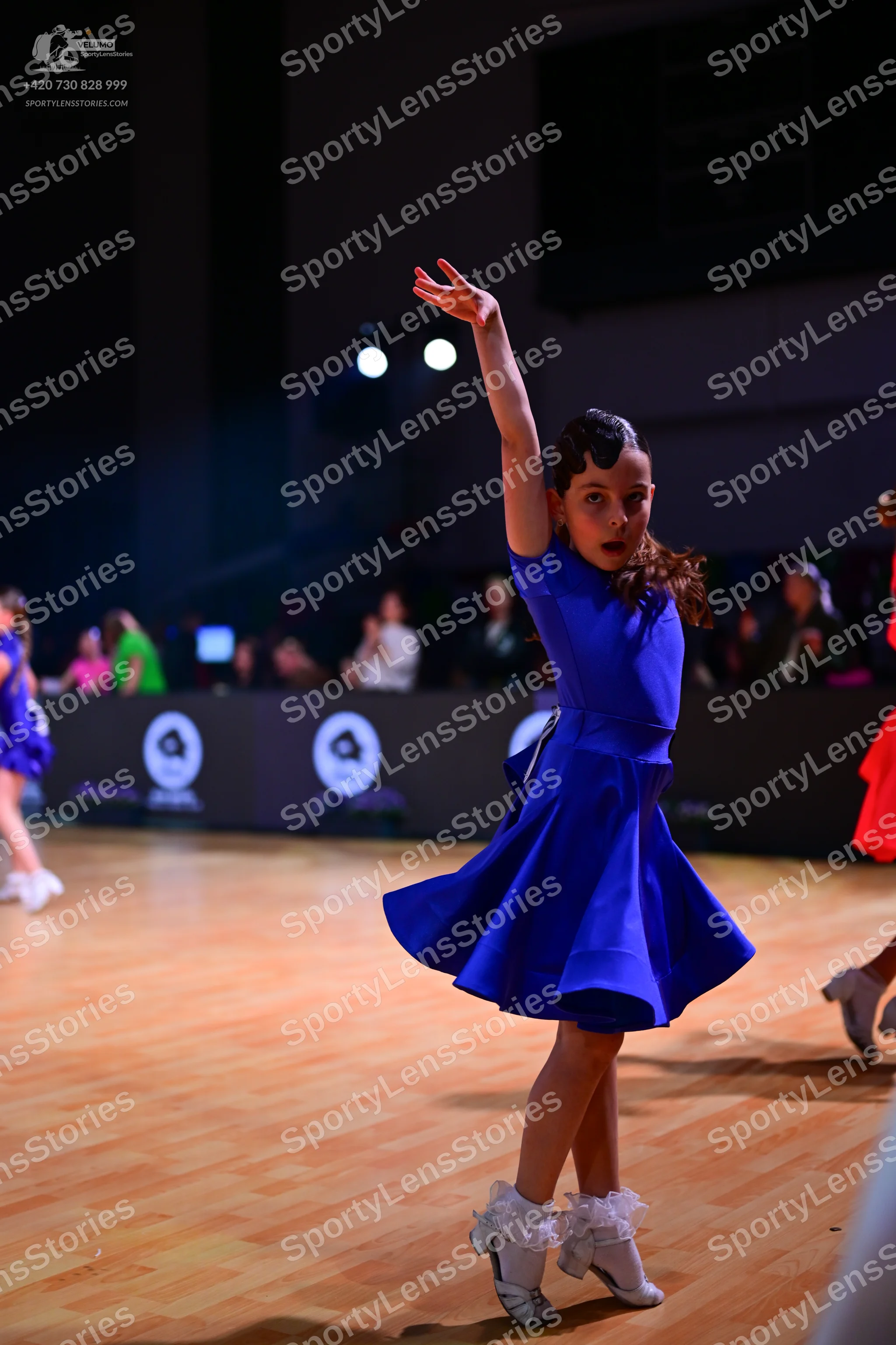 Dancesport competitor: Female dancer in center: royal blue short-sleeved dress with a flared skirt and