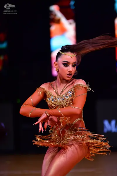 Dancesport competitor: Female dancer: gold/bronze Latin dance dress with sequins, crystals, and long fr